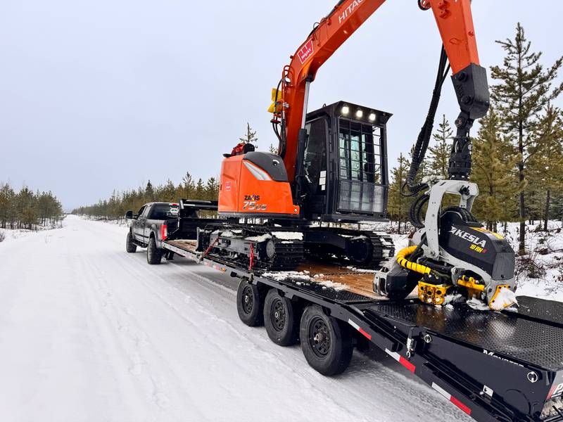 Compact Hitachi forestry harvester and Kesla head secured on a trailer on a snowy road